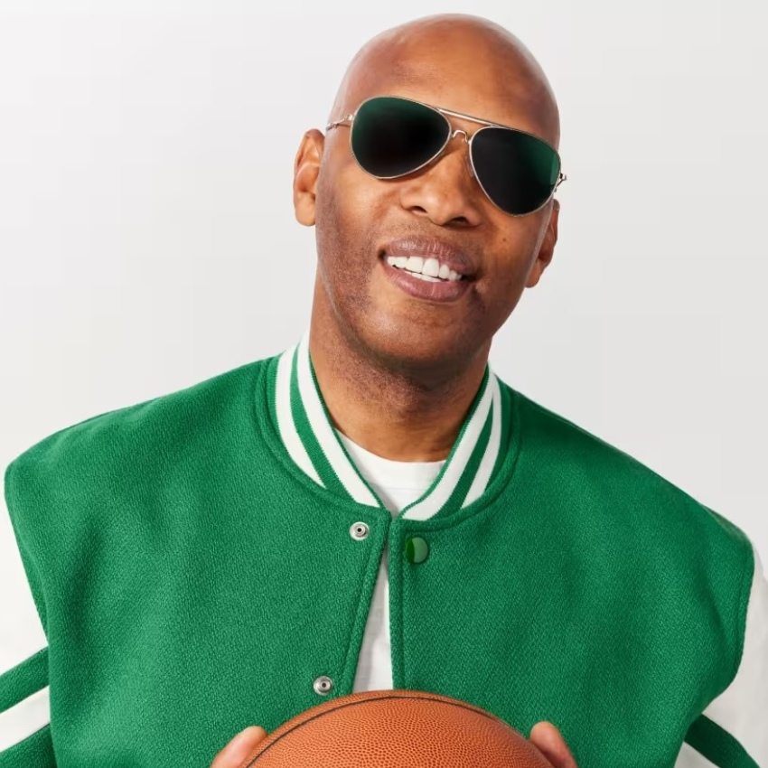 Person wearing a green varsity jacket with white stripes, holding a basketball and wearing sunglasses.