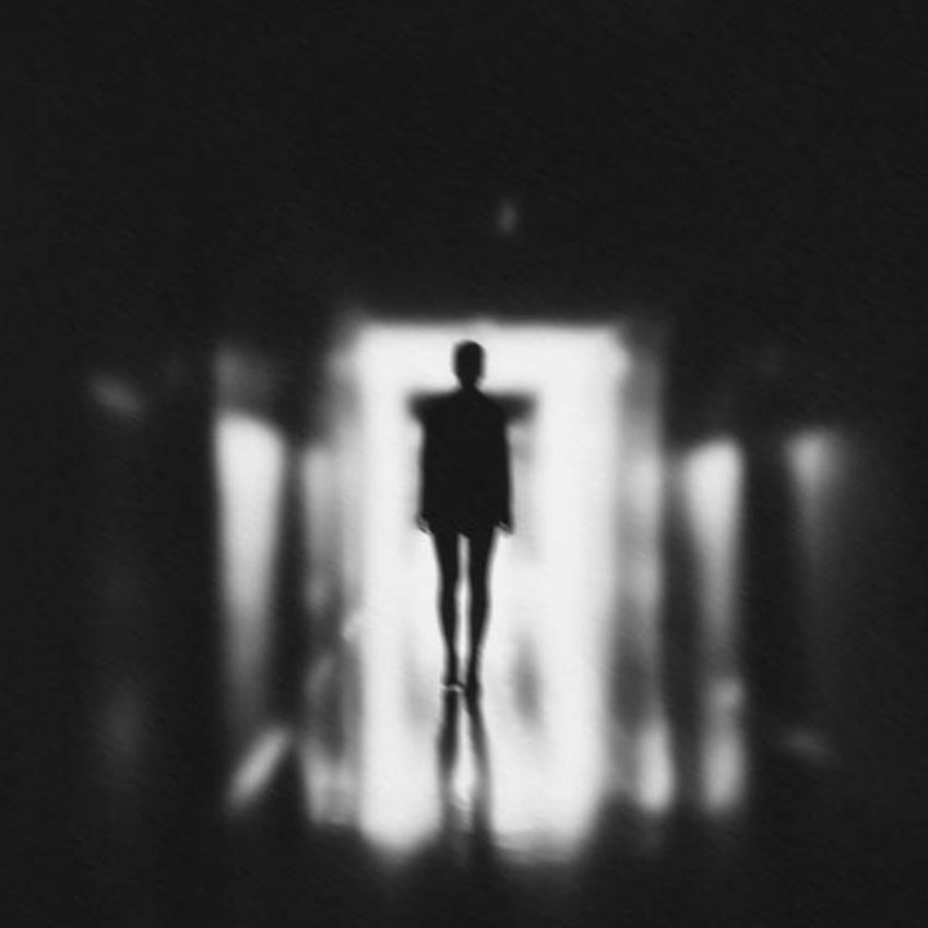 Silhouette of a person standing in a dimly lit corridor with light illuminating them from behind.