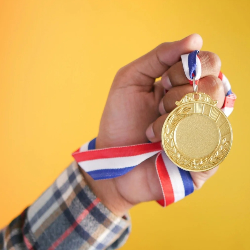 Hand holding a gold medal with a red, white, and blue ribbon.