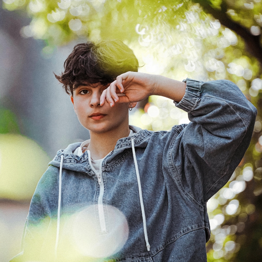 Person wearing a denim jacket with a hoodie, standing outdoors.