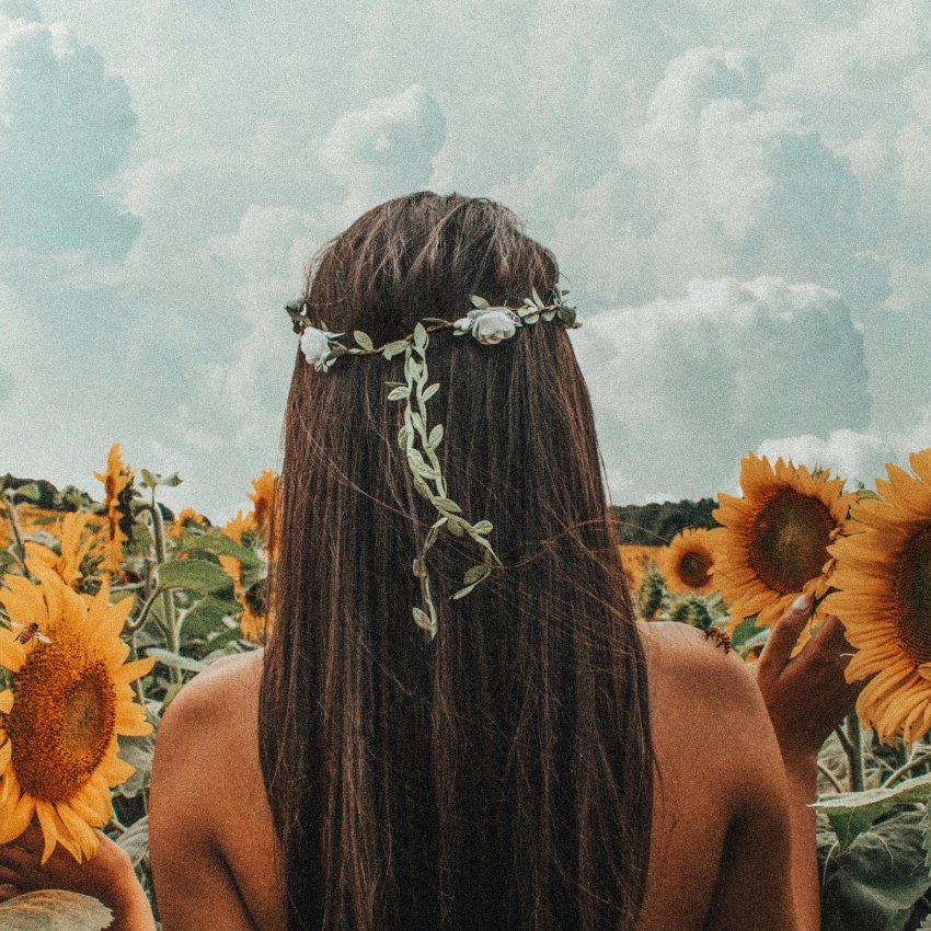 Person wearing a floral crown, standing in a sunflower field, facing away from the camera.