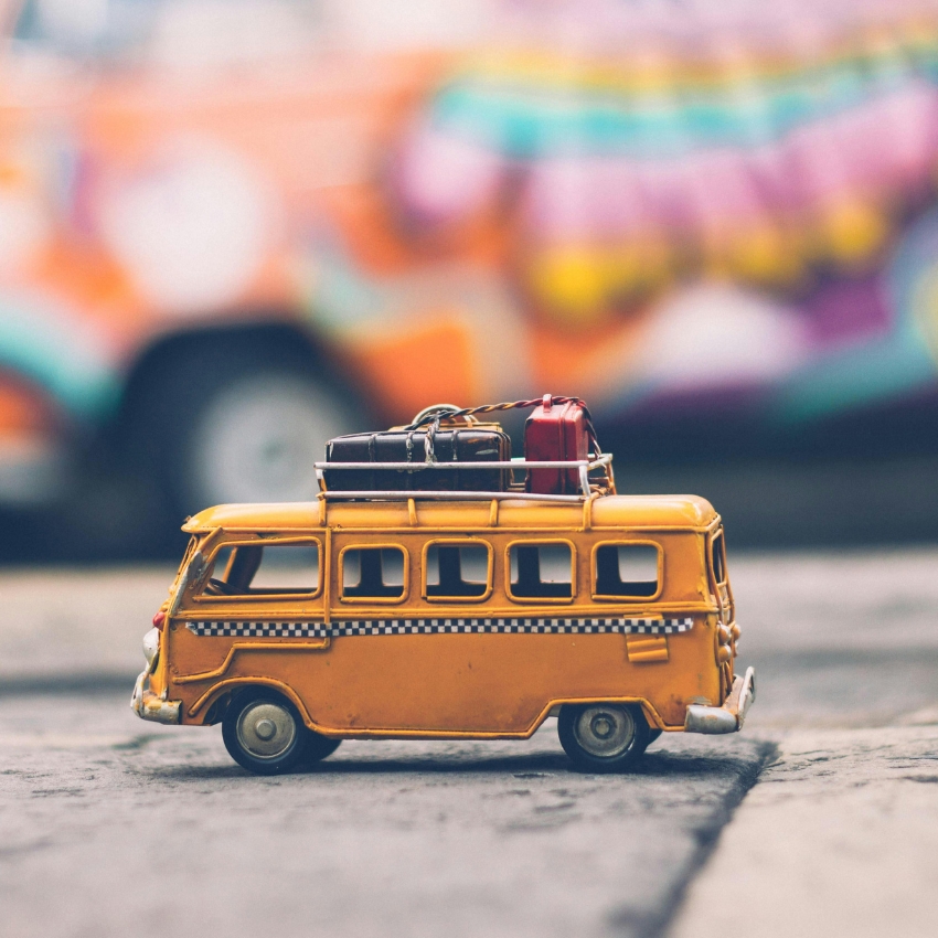 Yellow toy van with checkered stripe and luggage on top.