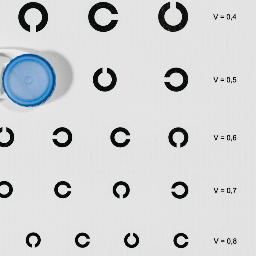 Eye chart with a blue bottle cap covering the first symbol; symbols are black with values V = 0.4 to V = 0.8.