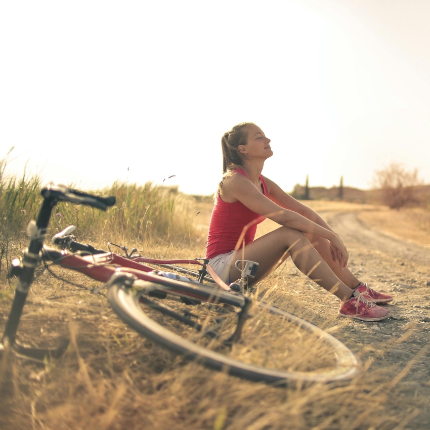 Person in athletic wear sits beside a road bike, resting on a trail with a serene expression.