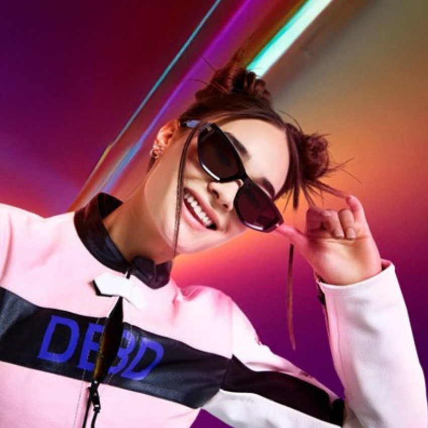 Woman wearing sunglasses and a pink jacket with "DEBD" written in blue on the front.