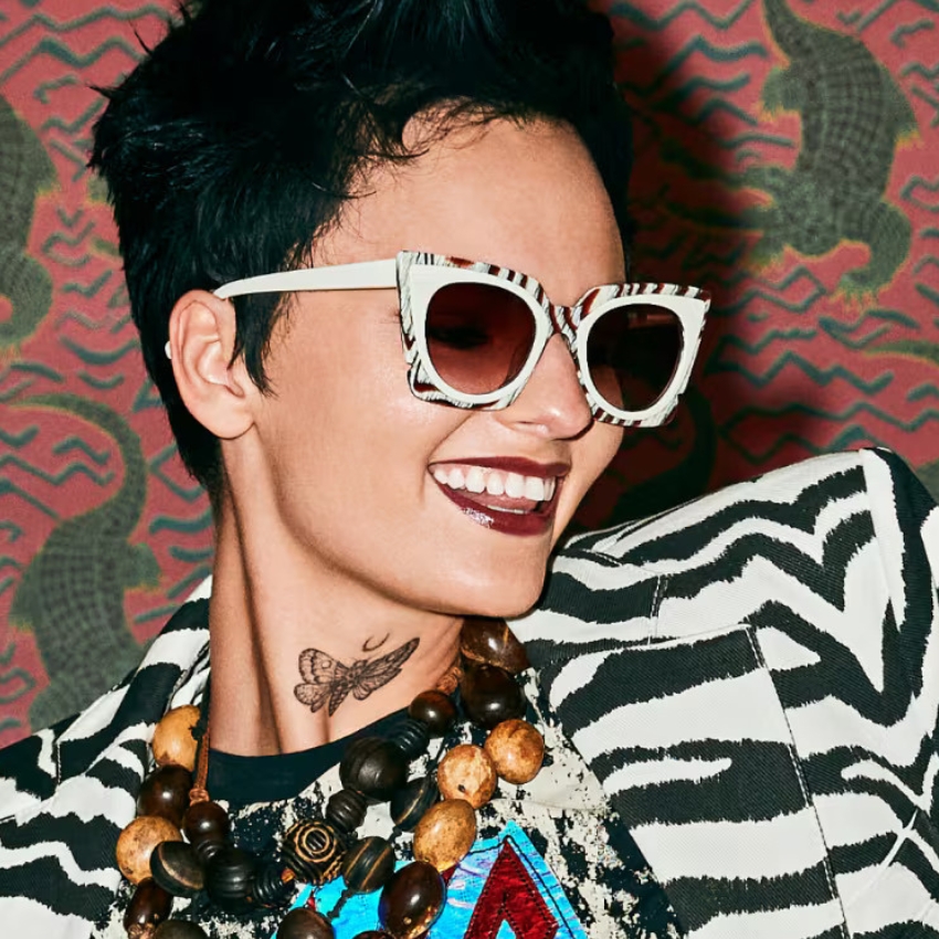 Woman wearing zebra-patterned sunglasses, matching zebra-striped jacket, and a beaded necklace.