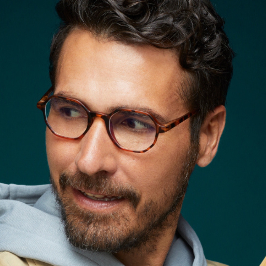 Man wearing tortoiseshell glasses with a clear, blue-tinted lens and a light gray hoodie.