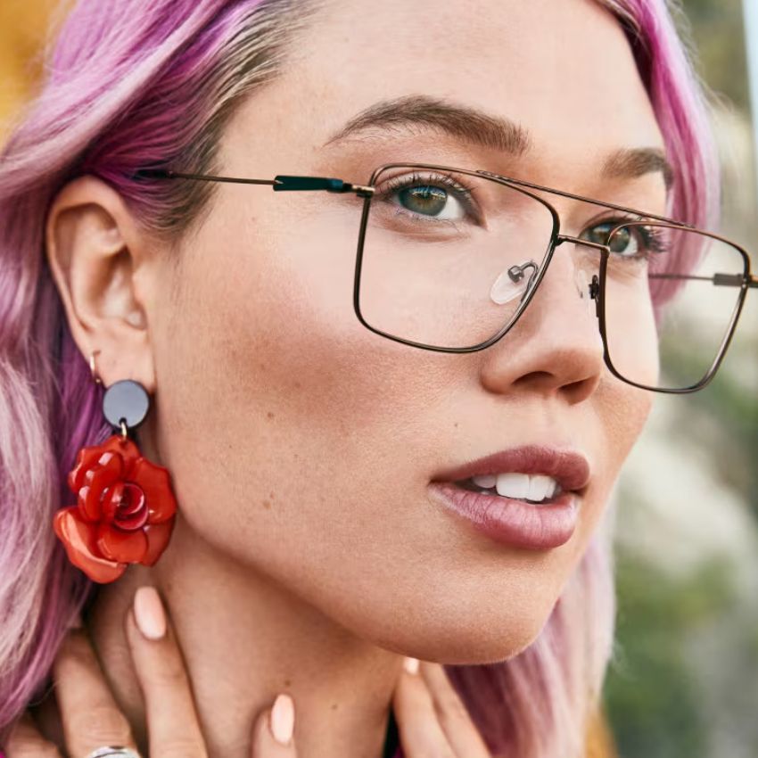 Woman wearing thin rectangular glasses and large red flower earrings.