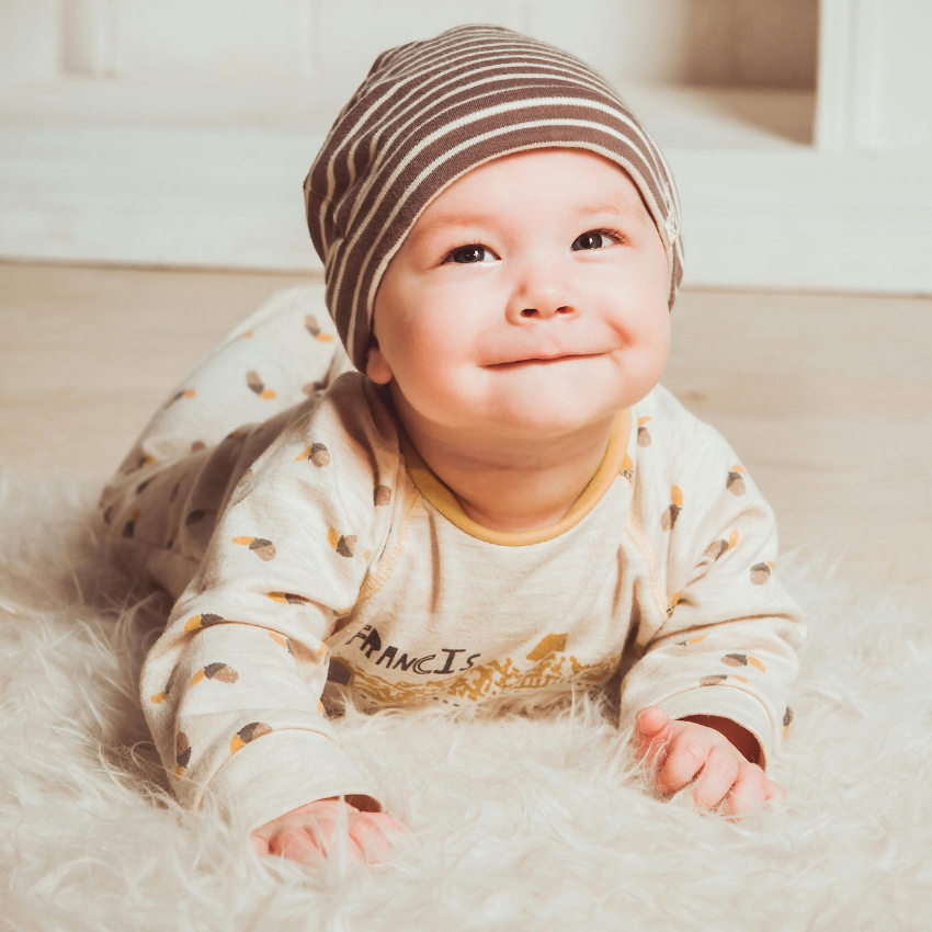 Baby wearing a striped hat and spotted pajamas, laying on a furry rug.