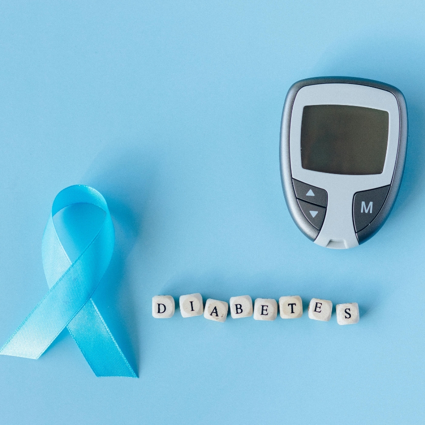 Blood glucose meter, blue ribbon, and letter cubes spelling "DIABETES" on a light blue background.