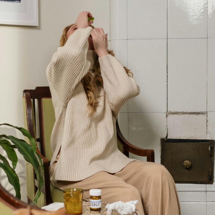 Person using nasal spray near table with Allergy medication bottle.