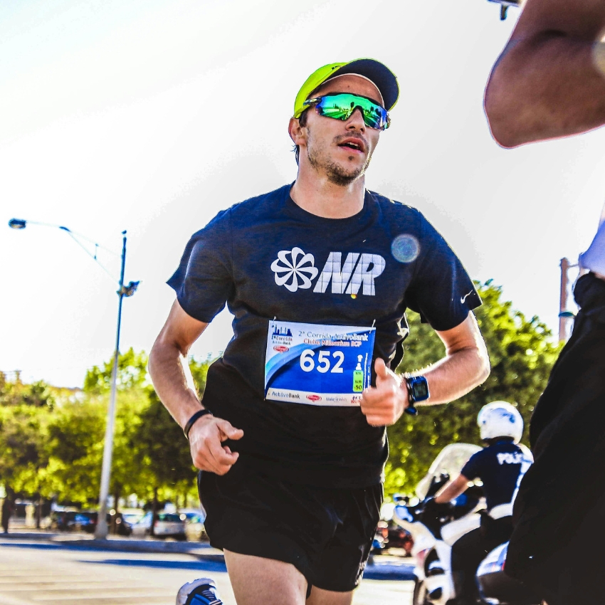 Runner wearing sunglasses and a yellow hat in a marathon, bib number 652 and the shirt has the letters “MR”.