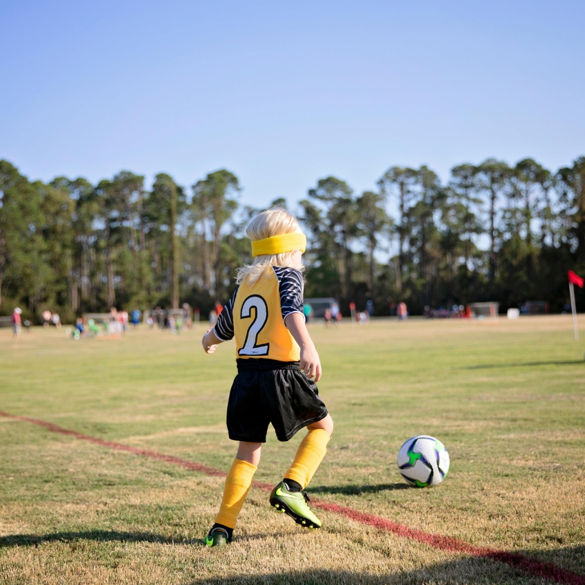 Child wearing a yellow and black jersey with the number 2, playing soccer on a grassy field.