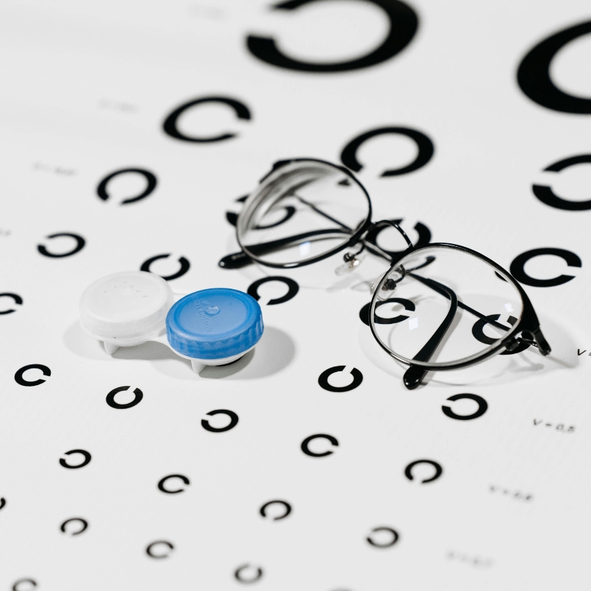 Contact lens case with blue and white caps and round eyeglasses on a vision test chart with large black C's.