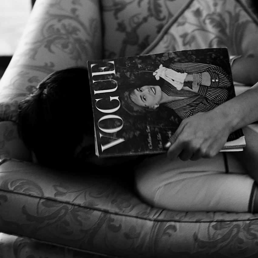 Person holding a Vogue magazine featuring a woman in a striped outfit and white gloves on the cover.