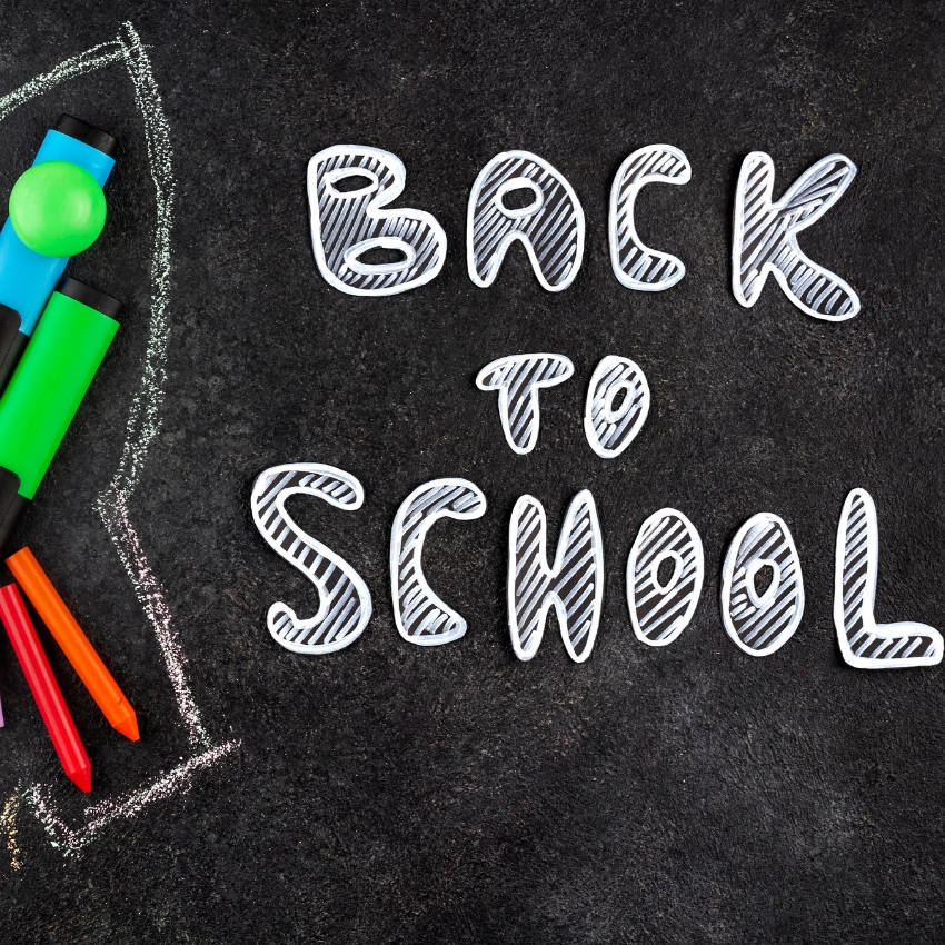 Back to School text on a blackboard with colorful markers and pencils.