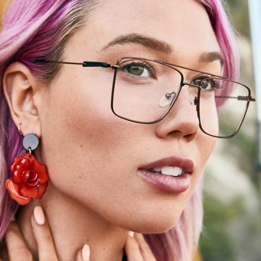 Person wearing large, square, thin-framed glasses and red rose-shaped earrings.