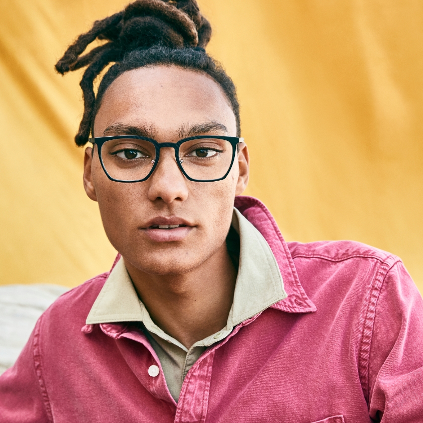 Person wearing black rectangular eyeglass frames and a pink shirt with a beige collar.