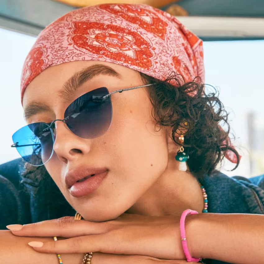 Woman wearing blue-tinted sunglasses, a red patterned headscarf, earrings, and a pink bracelet.