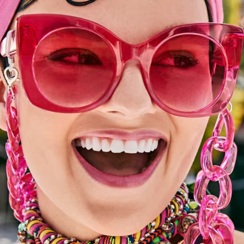 Woman wearing oversized pink sunglasses, colorful beaded necklace, and pink chain strap accessory.