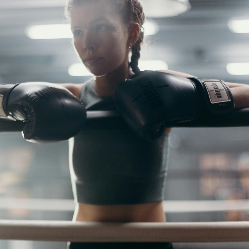 Woman in a gym wearing black boxing gloves branded "everlast" with "10 oz" written on the wrist strap.