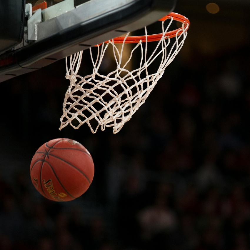 Basketball about to go through an orange hoop with white net.