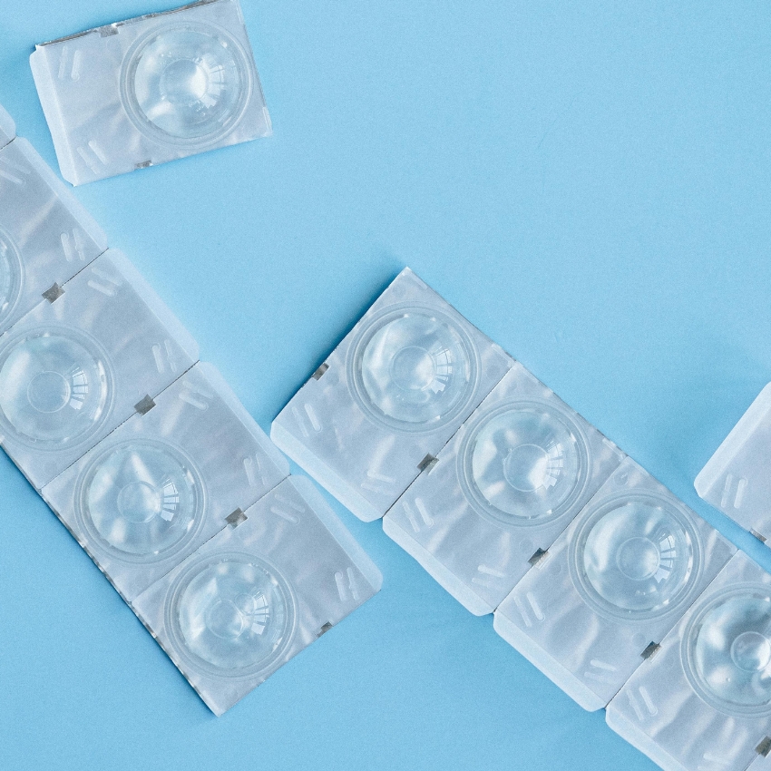 Contact lenses in blister packs arranged in a pattern on a light blue background.