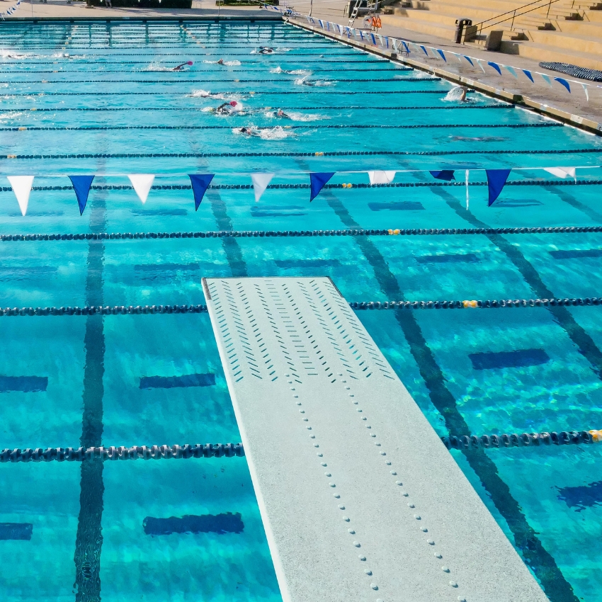 Diving board overlooking a swimming pool with lanes and swimmers.