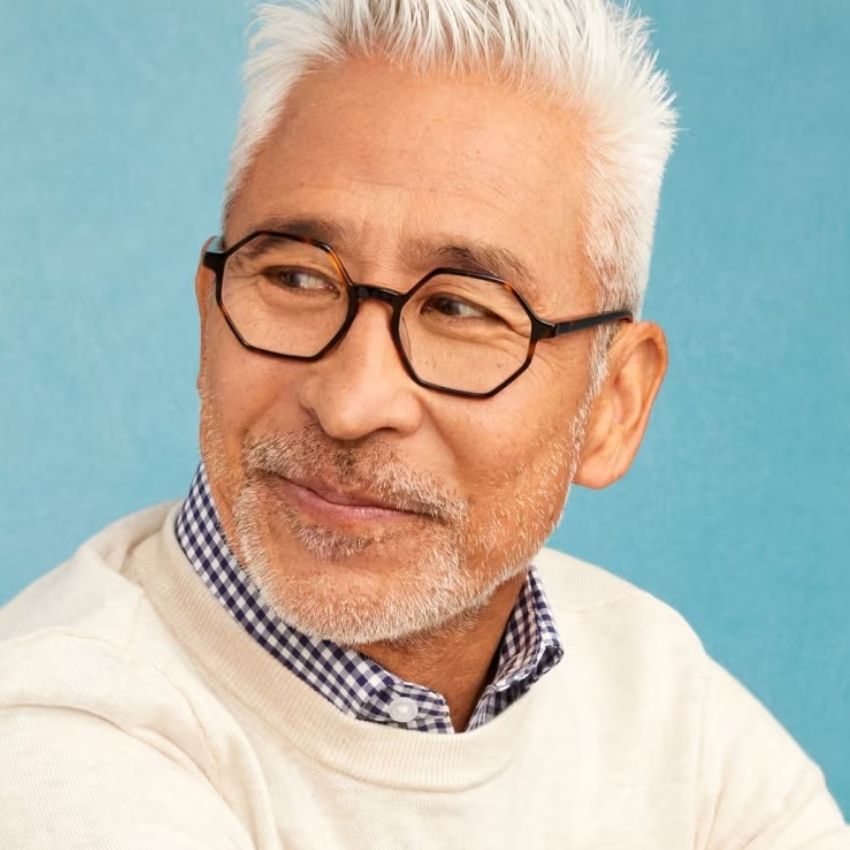 Man wearing hexagonal black-framed eyeglasses, he has white hair and a short beard.