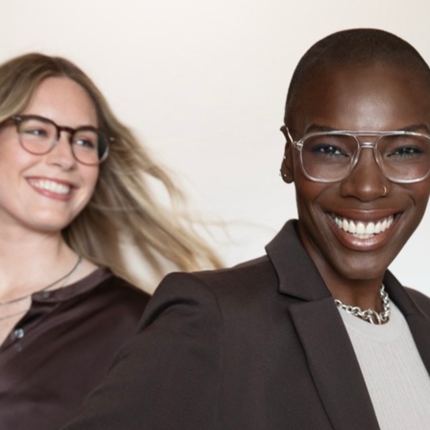 Two women wearing modern, stylish glasses and business attire, smiling confidently.