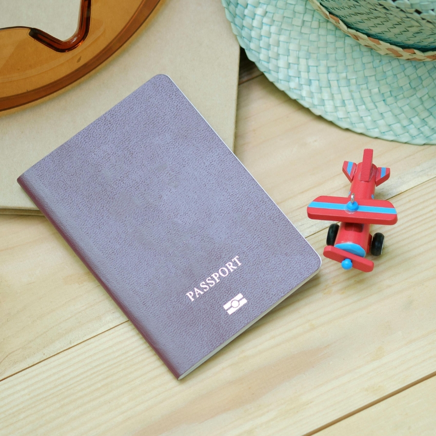 Passport next to a small red toy plane on a wooden surface.