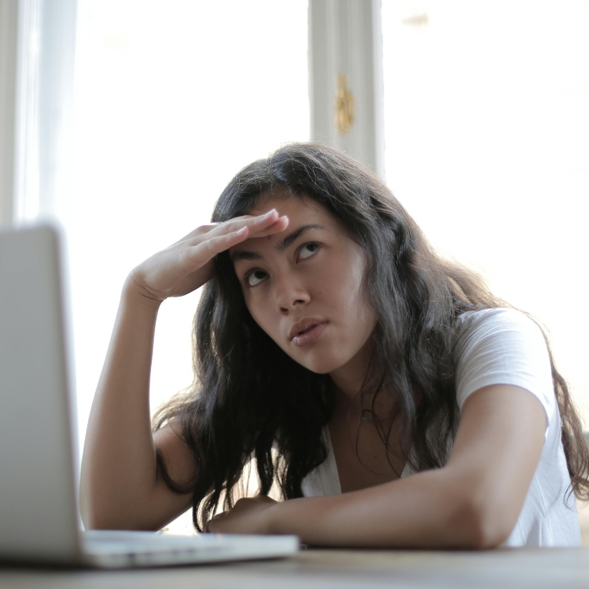 Woman with long hair shielding her eyes, looking at a laptop screen.