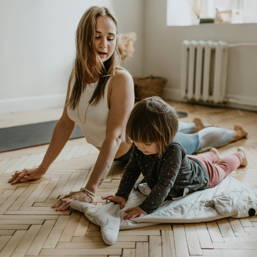 Woman and child doing yoga on hardwood floor. The child is on a mat shaped like a whale.