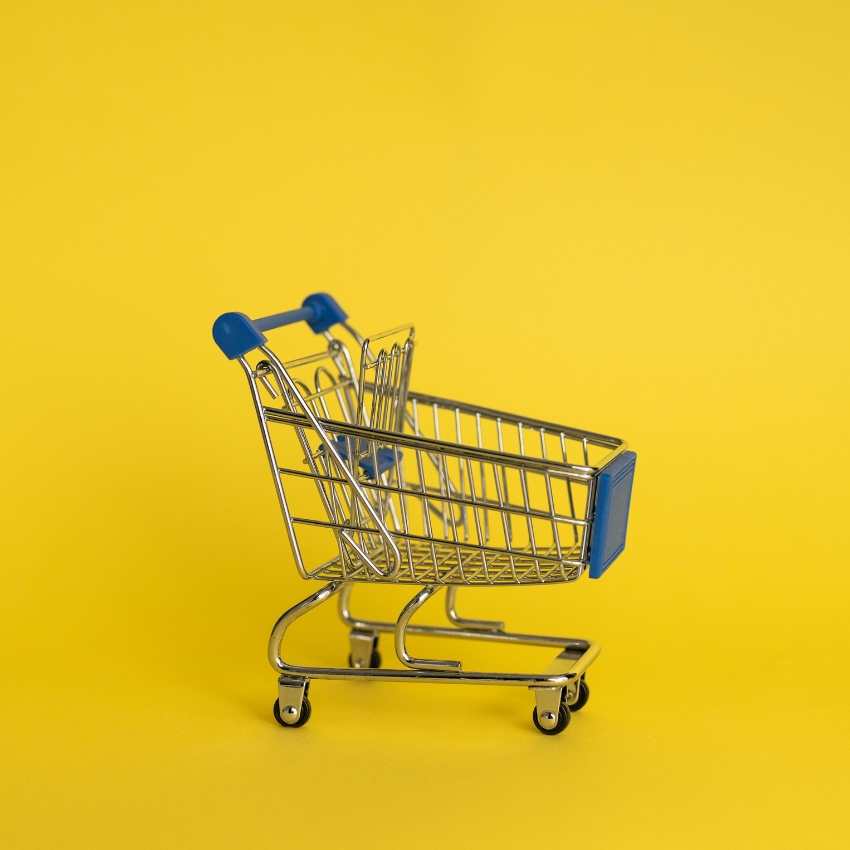 Small metal shopping cart with blue handle and accents on a yellow background.