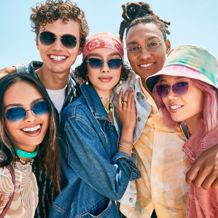 A group of five young people wearing stylish, colorful sunglasses, smiling and posing together.