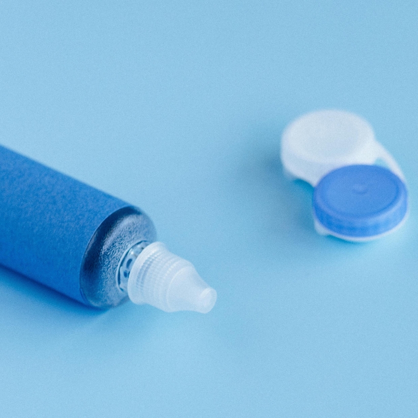 Eye drop bottle with a screw cap and an open contact lens case on a light blue background.