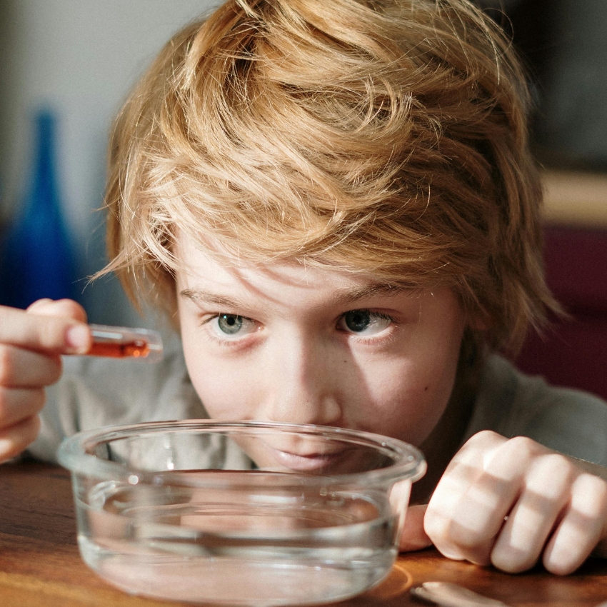 Child using a dropper to add liquid into a bowl of water.