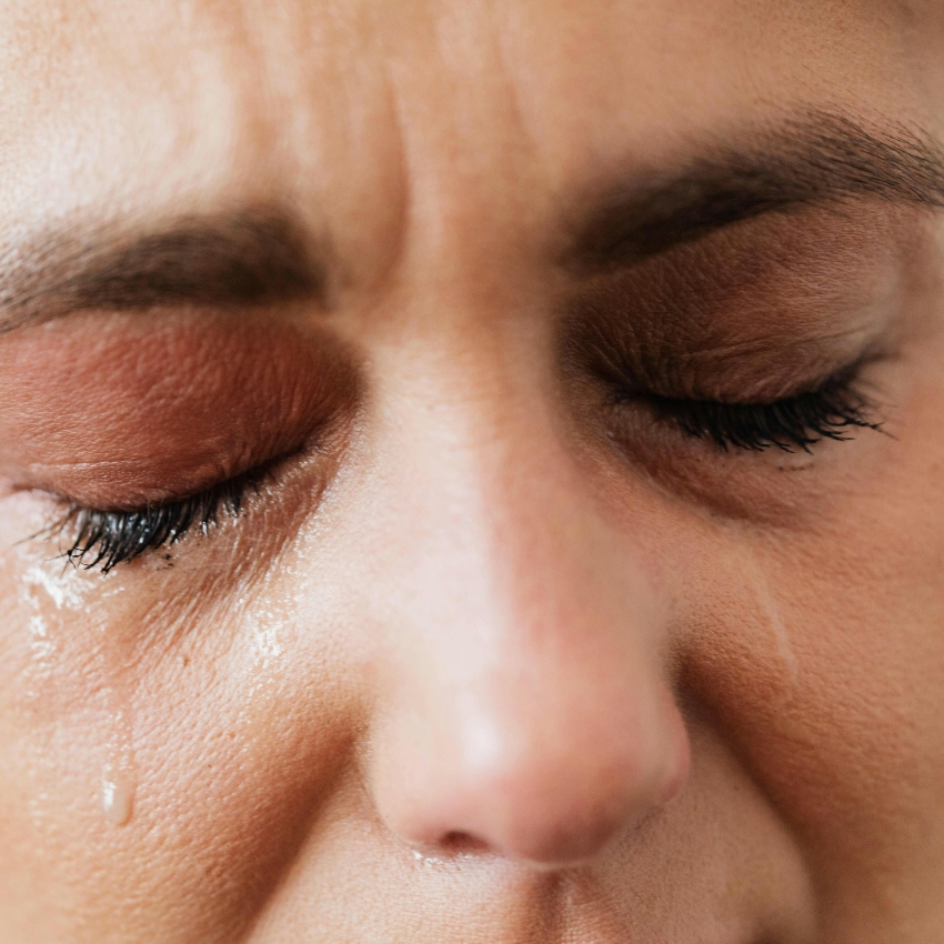 Close-up of closed eyes with mascara running and tears on cheeks.