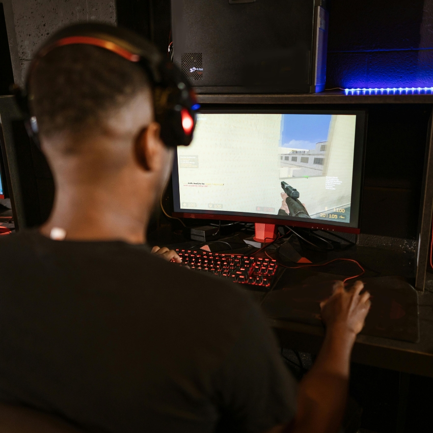 Person playing a first-person shooter game on a computer with a headset and a red backlit keyboard.