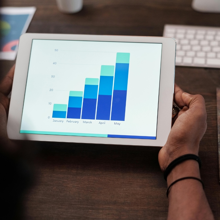 Hands holding a tablet displaying a bar chart with months January to May and values 0 to 50.