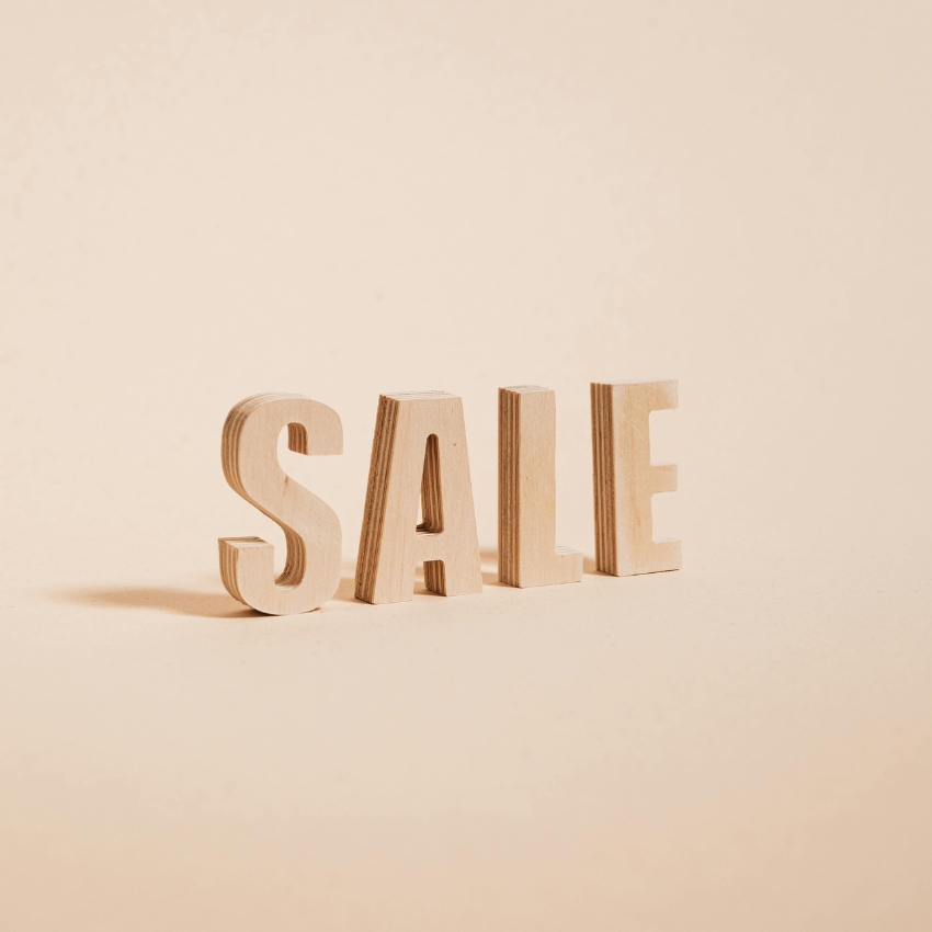 Wooden block letters spelling "SALE" on a beige background.