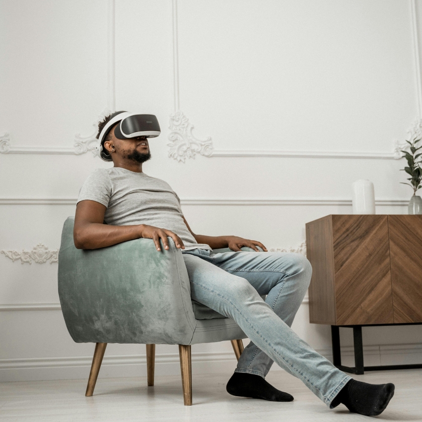 Person seated, wearing gray VR headset, gray shirt, and light blue jeans.