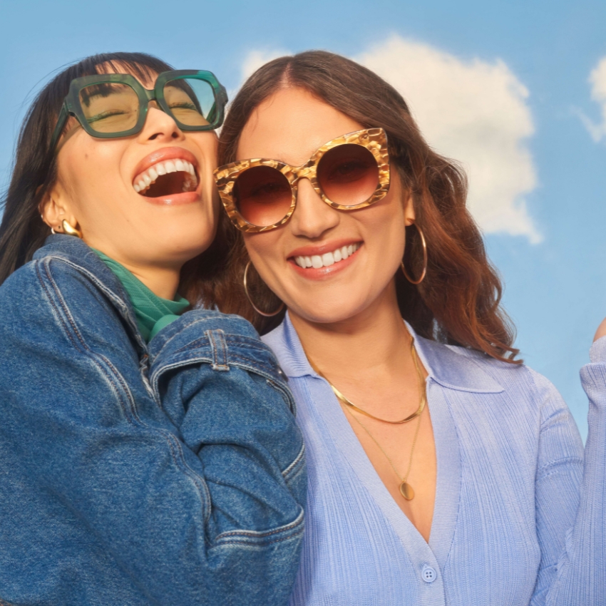 Women wearing stylish sunglasses: one with large square green frames, the other with round tortoiseshell frames.