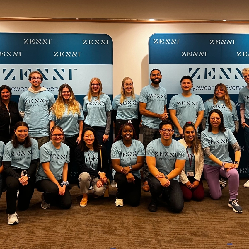 Zenni employees wearing matching shirts in front of a Zenni banner. Shirts say "Zenni Eyewear for Everyone."