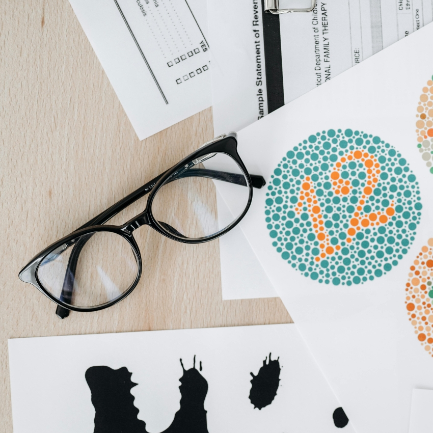 Black eyeglasses on a table with a colorblindness test showing the number 12.