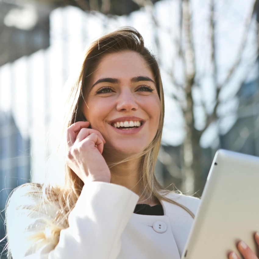 Smiling person holding a tablet outdoors.