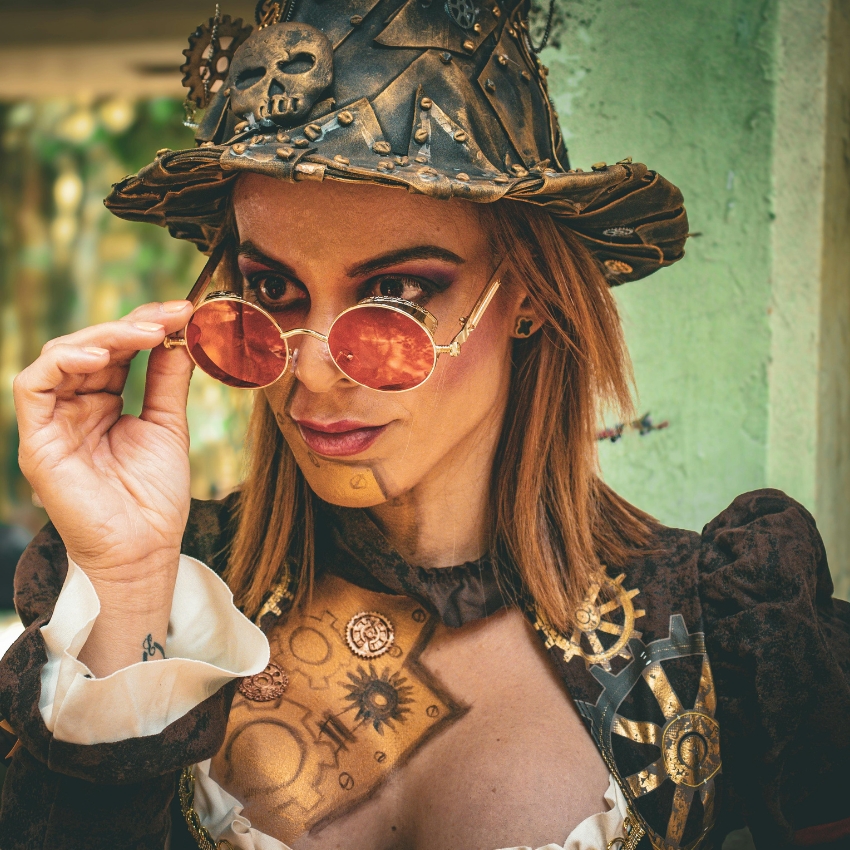 Steampunk hat with gears and skull, worn with round tinted glasses.