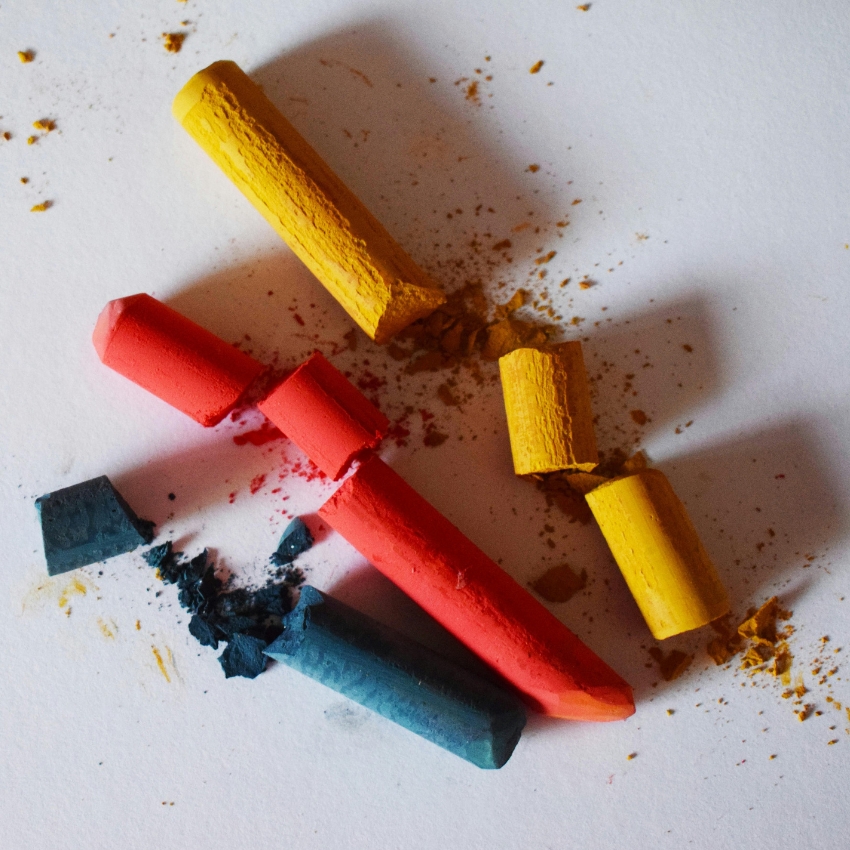 Red, yellow, and blue pastel sticks on white paper with scattered crumbs.