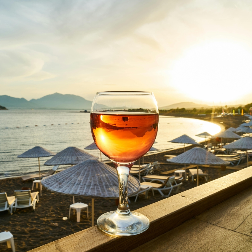 Glass of rosé wine on a wooden ledge with a beach in the background.