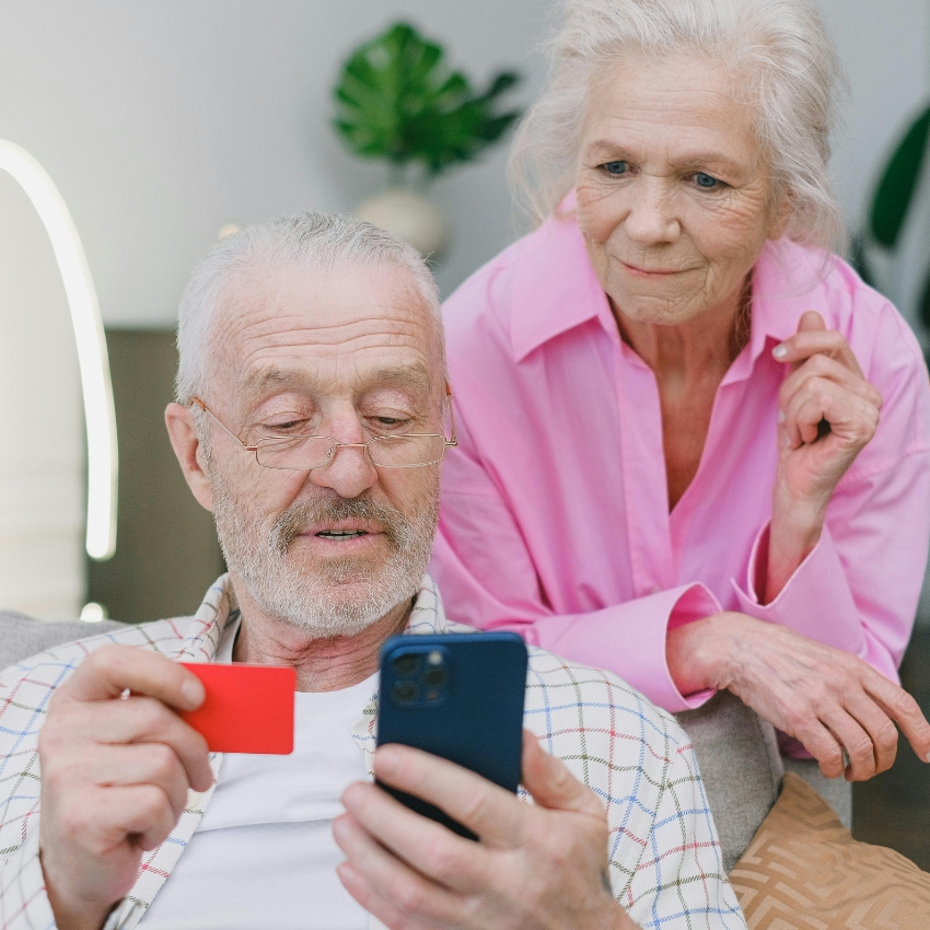 Elderly man holding a red card and a smartphone.